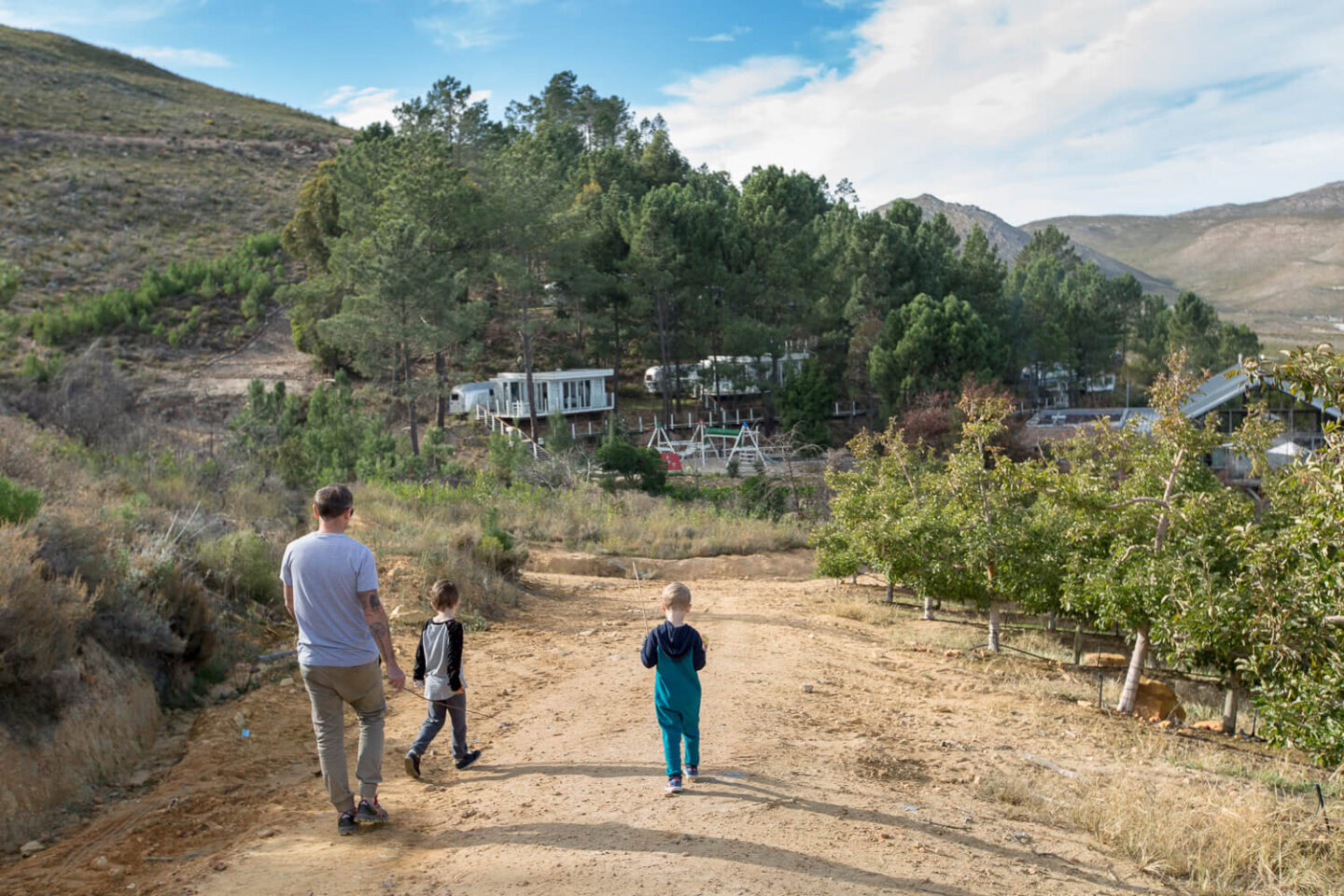 Activities A man and two boys walking up a dirt road between apple trees towards the Airstreams on the hillside, Old Mac Daddy, Elgin Valley