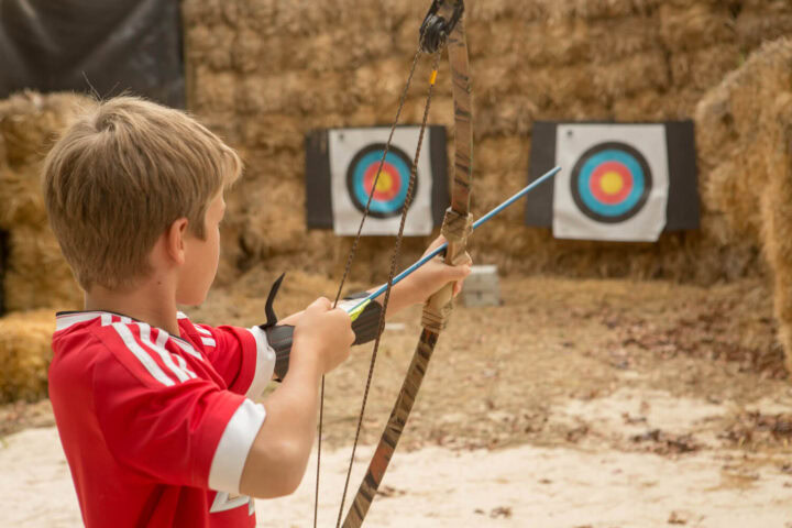 A boy aiming a bow at a target set against hay bales, Old Mac Daddy, Elgin Valley