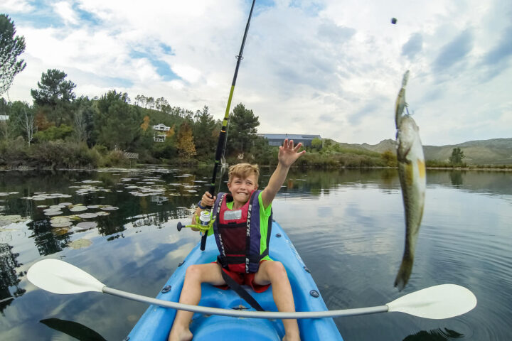 A boy in a kayak holding up a fish he has just caught, Old Mac Daddy, Elgin Valley