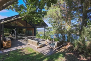 Apple Grove: the lodge from the lawn, with outdoor sofas and a wine barrel on the deck among the trees, Old Mac Daddy, Elgin Valley