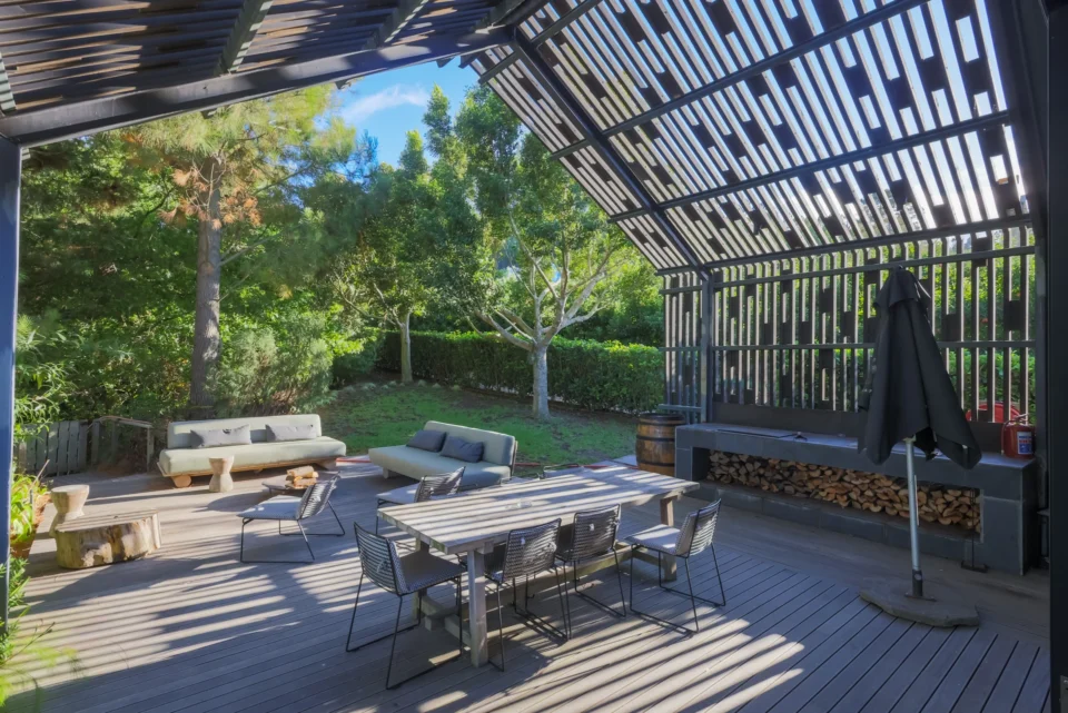 Apple Grove: dining table on the deck under the steel pergola, with a log store and garden behind, Old Mac Daddy, Elgin Valley