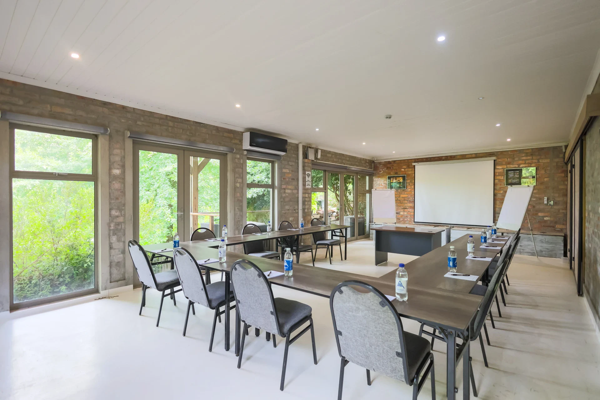 Home The conference room laid out in a U-shape with upholstered chairs, a projector screen and flip chart, garden through the windows, Old Mac Daddy, Elgin Valley