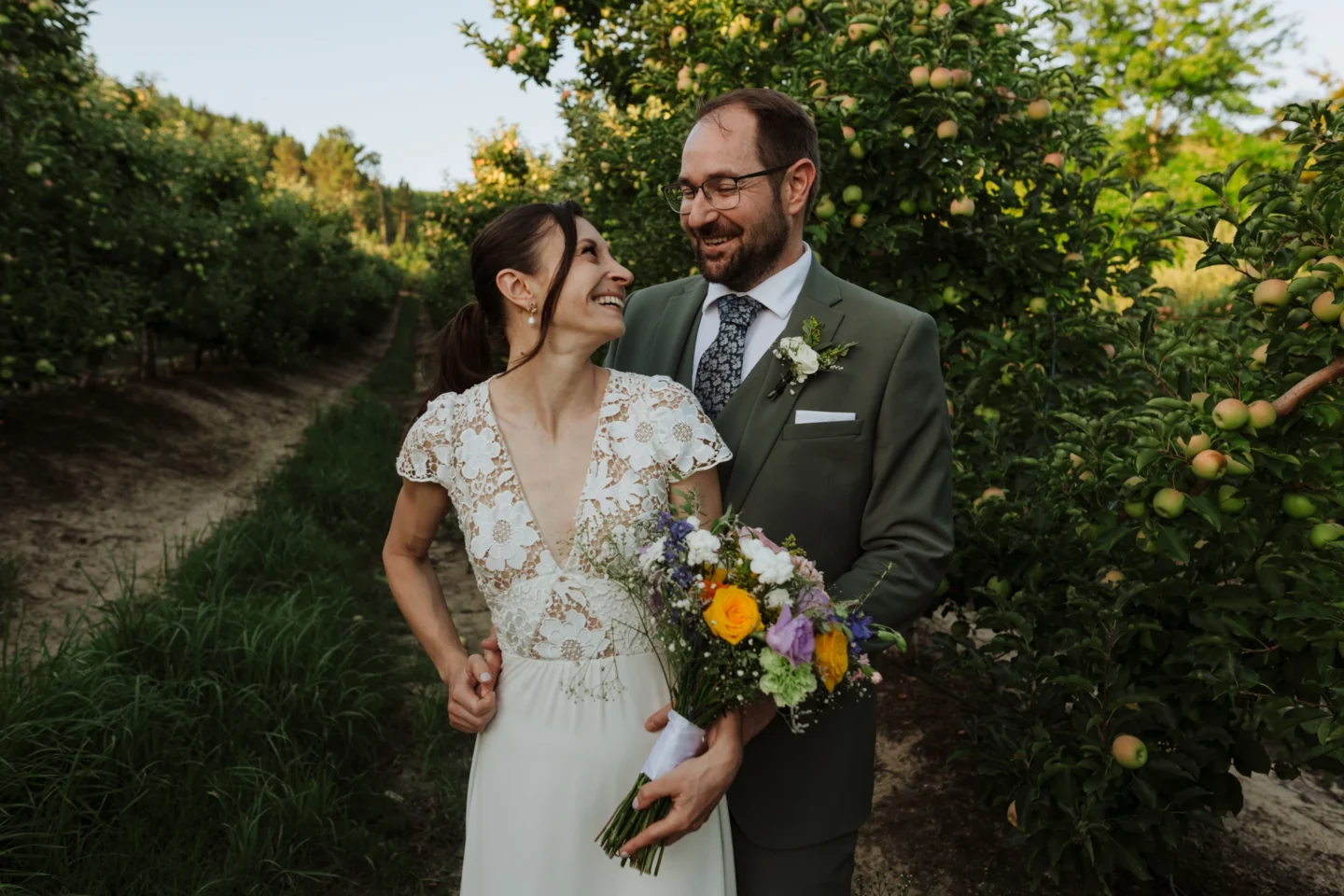 Bride and groom smiling at each other among the apple trees, a colourful bouquet in her hand, Old Mac Daddy, Elgin Valley