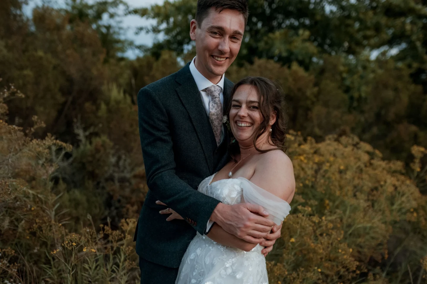 Groom with his arms around the bride, both smiling, among the fynbos in the evening light, Old Mac Daddy, Elgin Valley