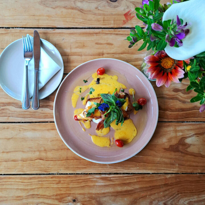 A plated dish with a yellow sauce, herbs and cherry tomatoes on a timber table, Old Mac Daddy, Elgin Valley