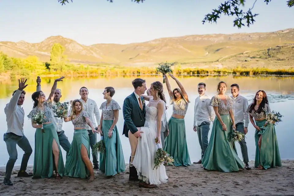 Weddings & Events (new) Bridal party celebrating on the lakeside beach, bouquets in the air, mountains across the water, Old Mac Daddy, Elgin Valley