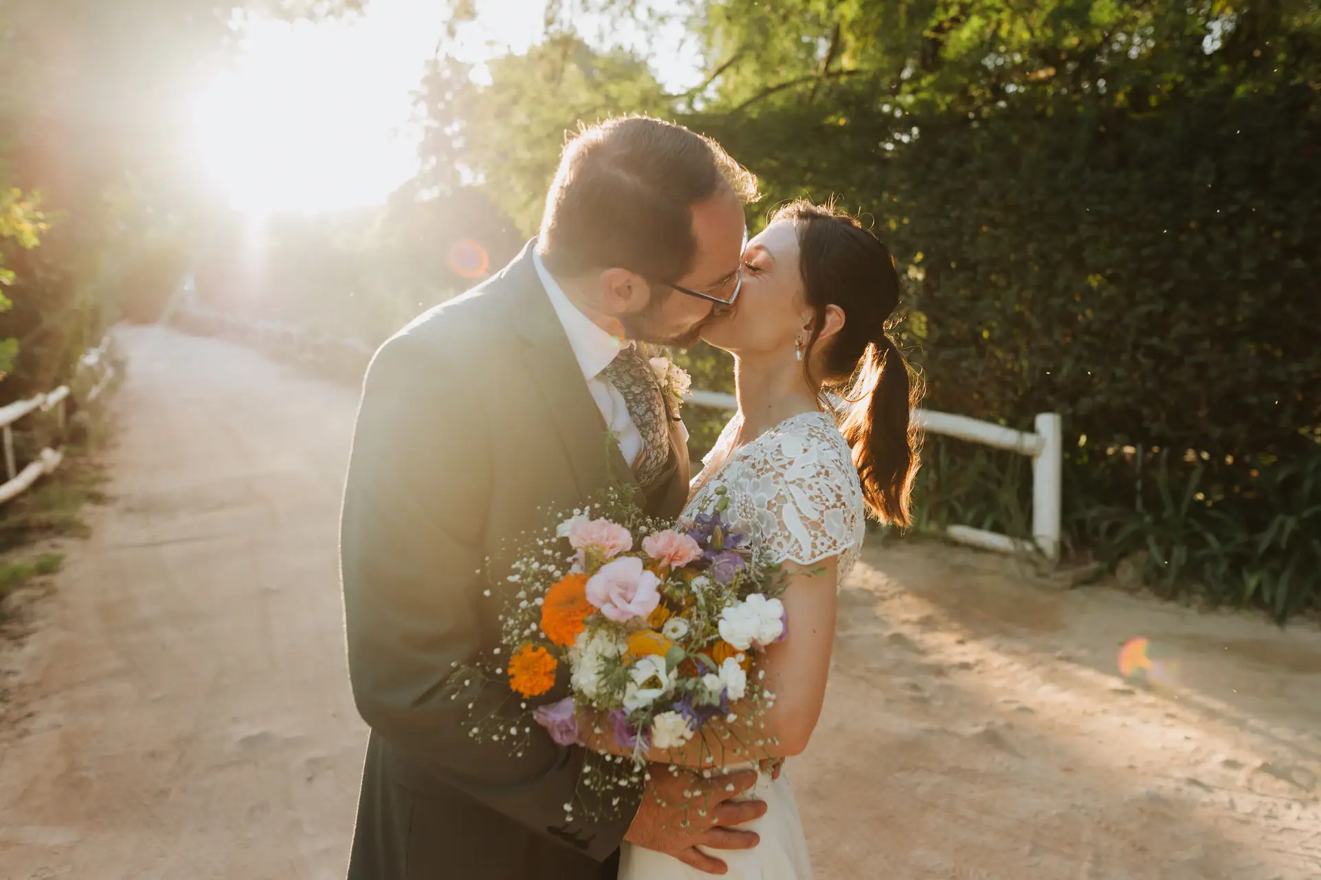 Home Bride and groom kissing on a sunlit lane, a wildflower bouquet in her hand, Old Mac Daddy, Elgin Valley